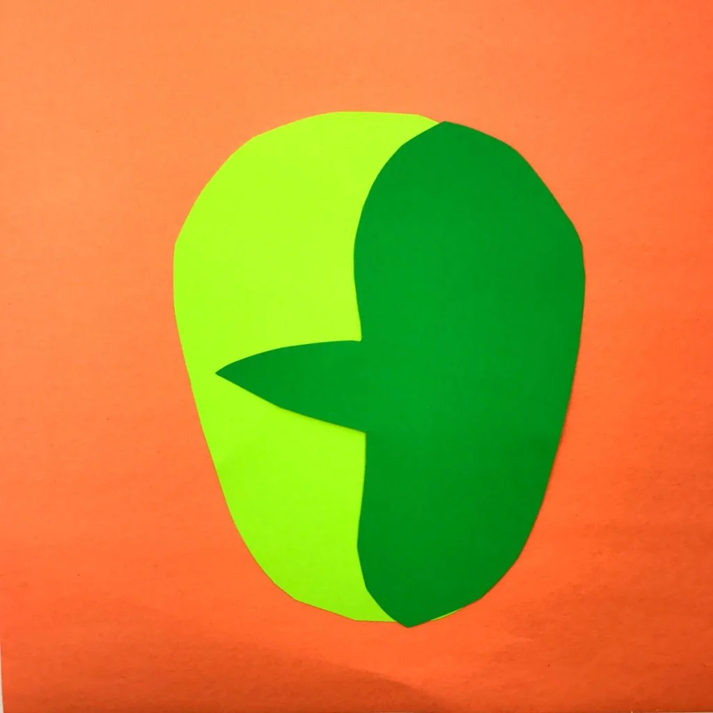 Full face shape is glued onto another sheet of construction paper and the cut out face profile has been glued on top