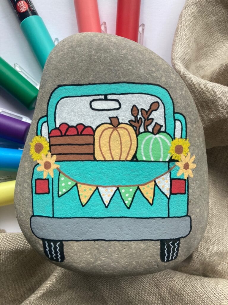 Fall Painted Rock Tutorial finished craft -a rock has the back of a truck painted on it that's filled with fall items like pumpkins and apples
