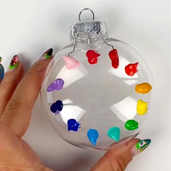 Rainbow of paint colors on an clear christmas tree ornament in blobs