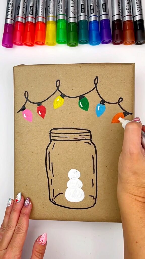 Adding the color to the Christmas lights on this DIY wrapping paper using paint markers. The white base color of the snowman has also been added to the jar,